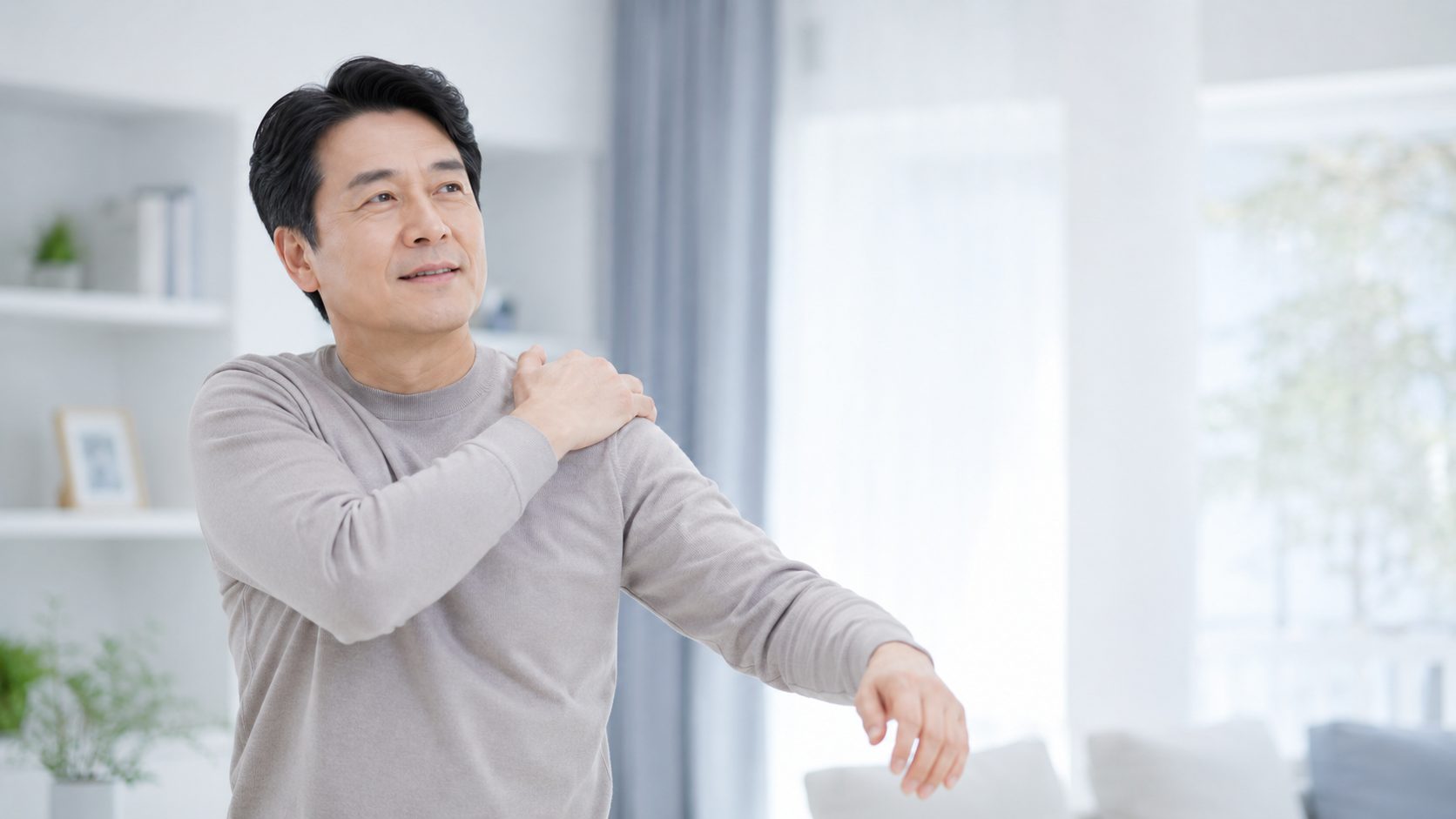 옷을 입으며 한쪽 팔을 천천히 들어 올리는 중년 남성